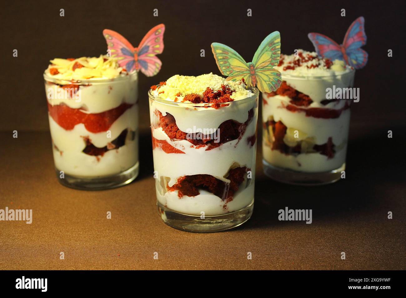 Trois parfaits dessert avec des décorations papillon, superposés de crème fouettée, de fraise et de chocolat sur un fond sombre Banque D'Images