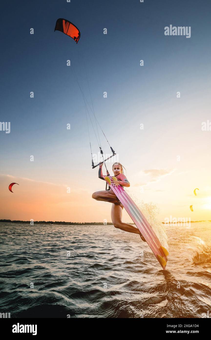 Grand angle. jeune femme caucasienne en combinaison fait un tour glissant sur l'eau contre la toile de fond d'un coucher de soleil dans la mer. Kitesurring Girl Banque D'Images