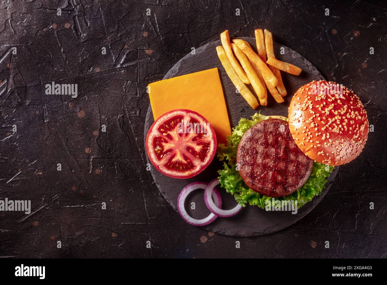 Ingrédients de hamburger, pris par le dessus sur le noir avec espace de copie.Délicieux steak de patty de bœuf avec frites et légumes Banque D'Images