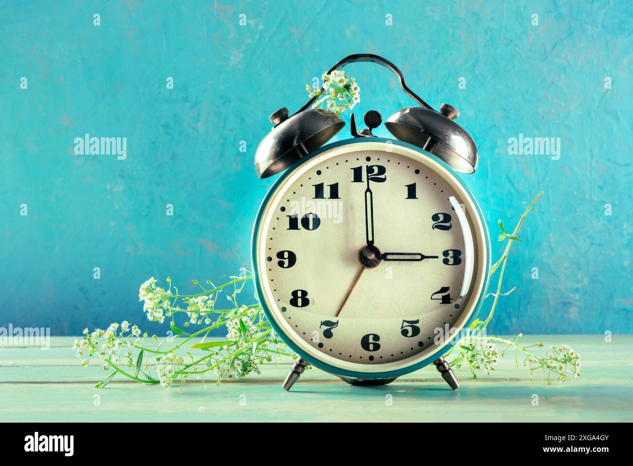 Concept d'heure d'été, printemps en avant.Un réveil vintage avec des fleurs fraîches sur un fond sarcelle avec un endroit pour le texte Banque D'Images