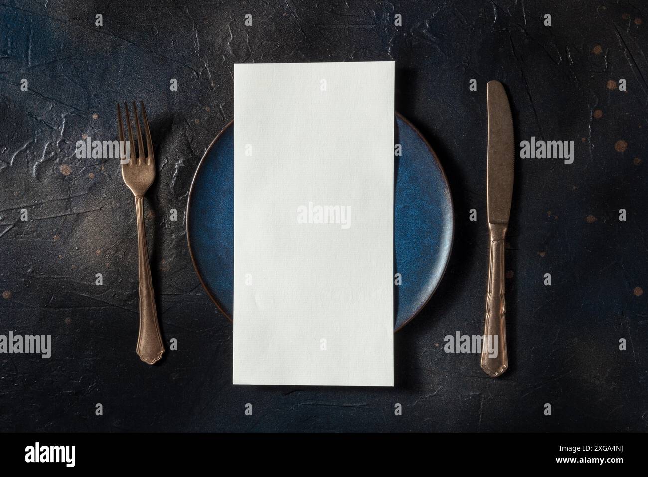 Menu du dîner ou concept d'invitation. Une fourchette, un couteau, et une plaque bleue avec une carte blanche, au-dessus de la tête plat, plan sur un fond noir Banque D'Images