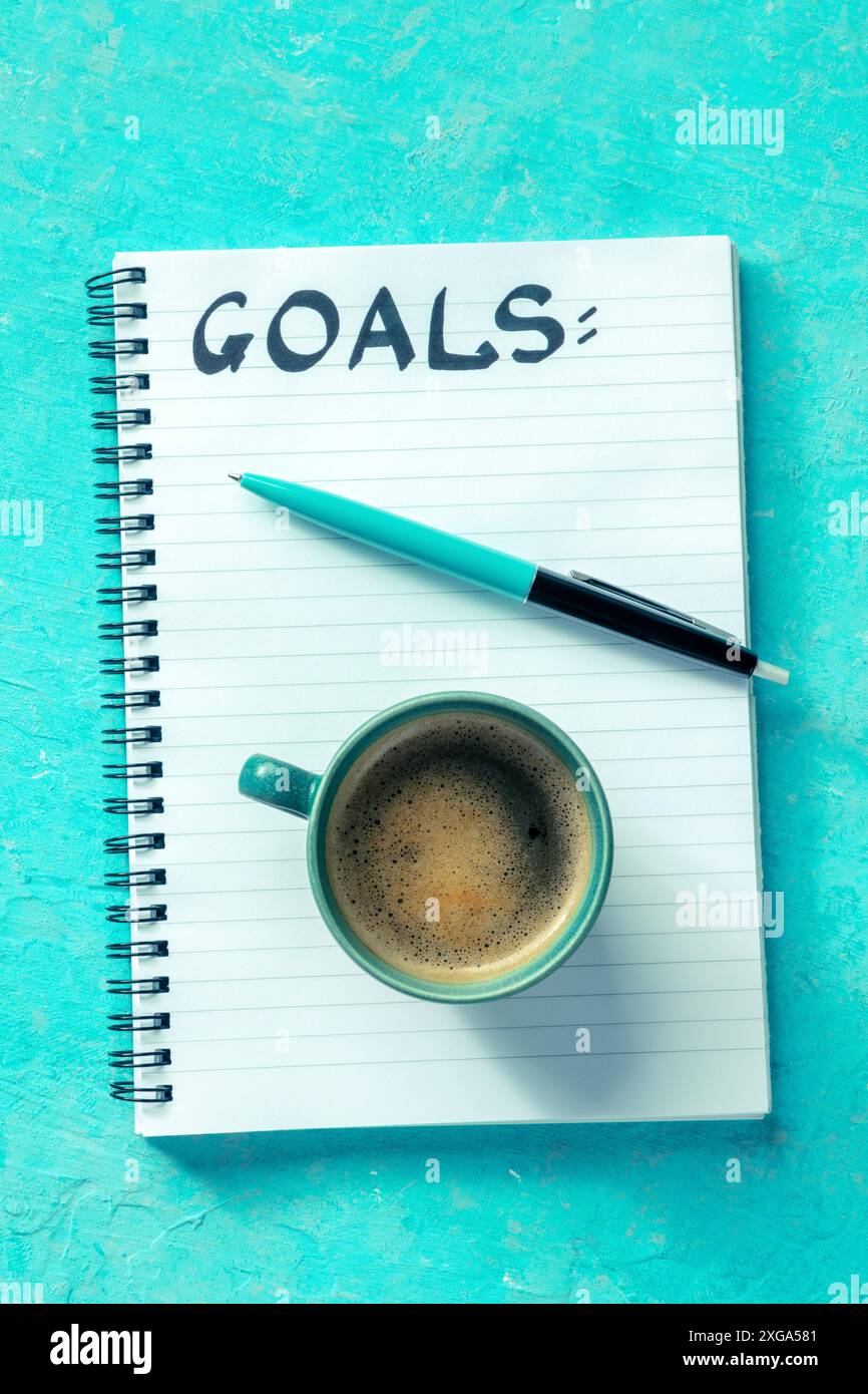 Définition des objectifs. Un cahier avec le mot manuscrit objectifs, avec une tasse de café et un stylo, plan suspendu sur un fond bleu vif. Le Banque D'Images