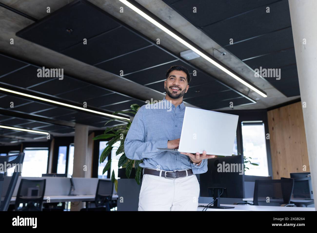 Tenant l'ordinateur portable, l'homme souriant avec confiance dans le bureau moderne, espace de copie Banque D'Images