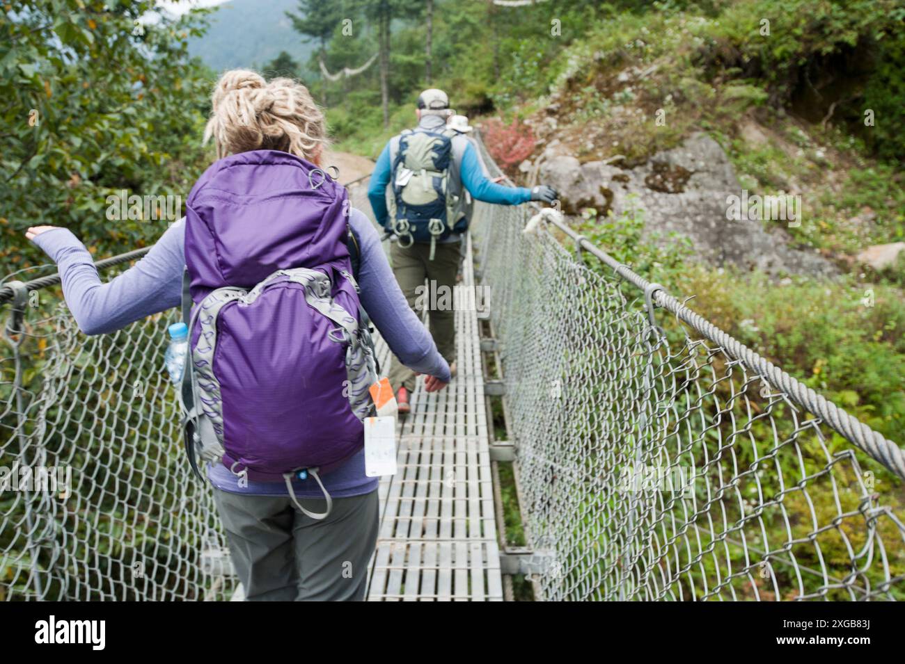 Un homme et une femme traversent un pont suspendu en métal fait par l'homme sur le trek vers Mt. Camp de base de l'Everest. Banque D'Images