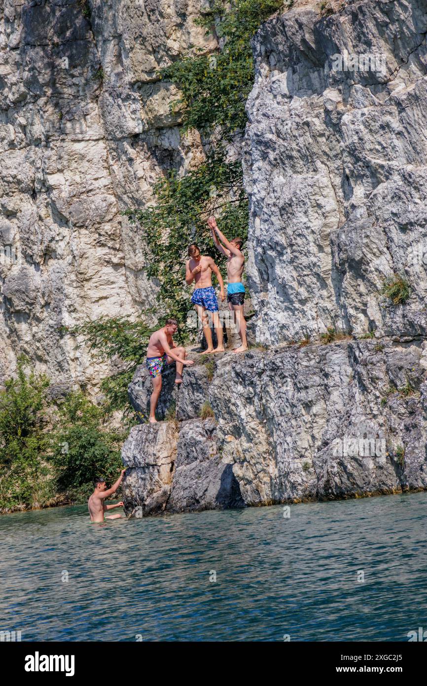 Par une chaude après-midi d'été au lac, les garçons plongent de la falaise dans l'eau. Banque D'Images