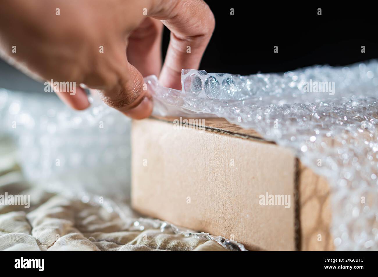 Gros plan de la main d'une personne enveloppant une boîte en carton avec du papier bulle pour la protection. Banque D'Images