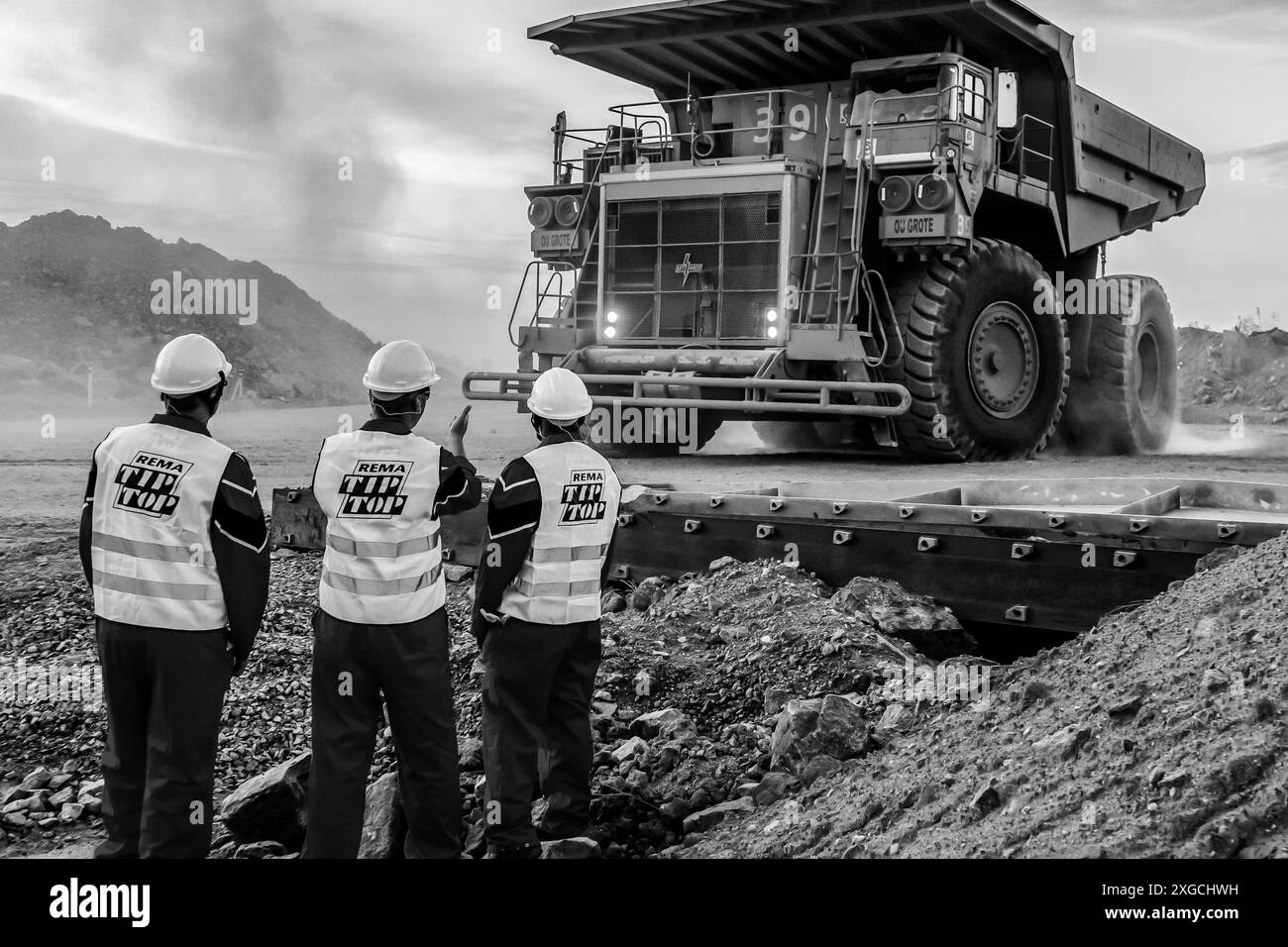 Une échelle de gris de trois inspecteurs de la sécurité minière examinant un gros camion à benne basculante transportant du minerai de palladium platine pour traitement en Afrique du Sud Banque D'Images