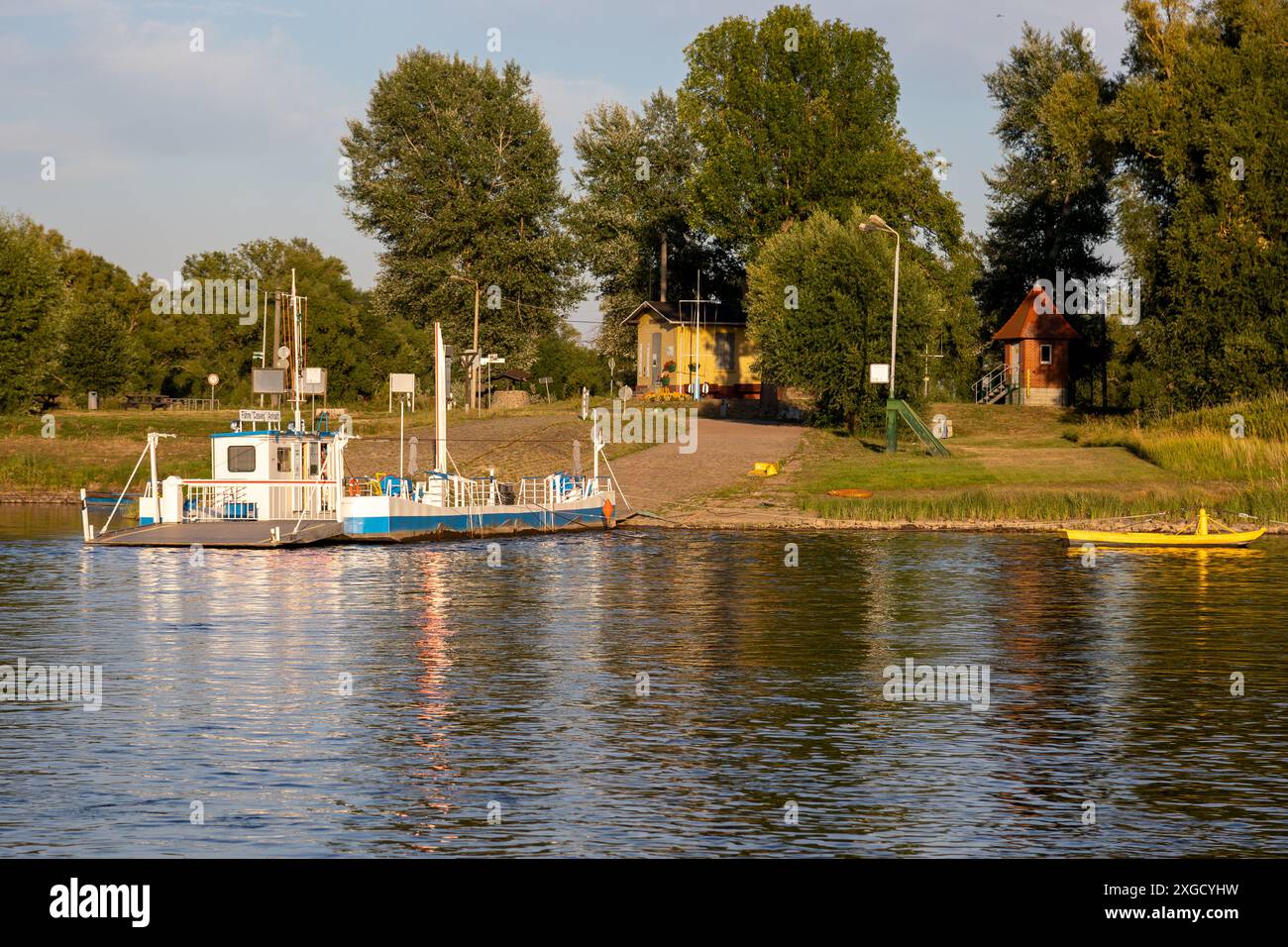 Le petit ferry traversant l'Elbe près de Coswig, en Allemagne, part d'un débarquement fluvial, laissant derrière lui un petit village et des arbres. Banque D'Images