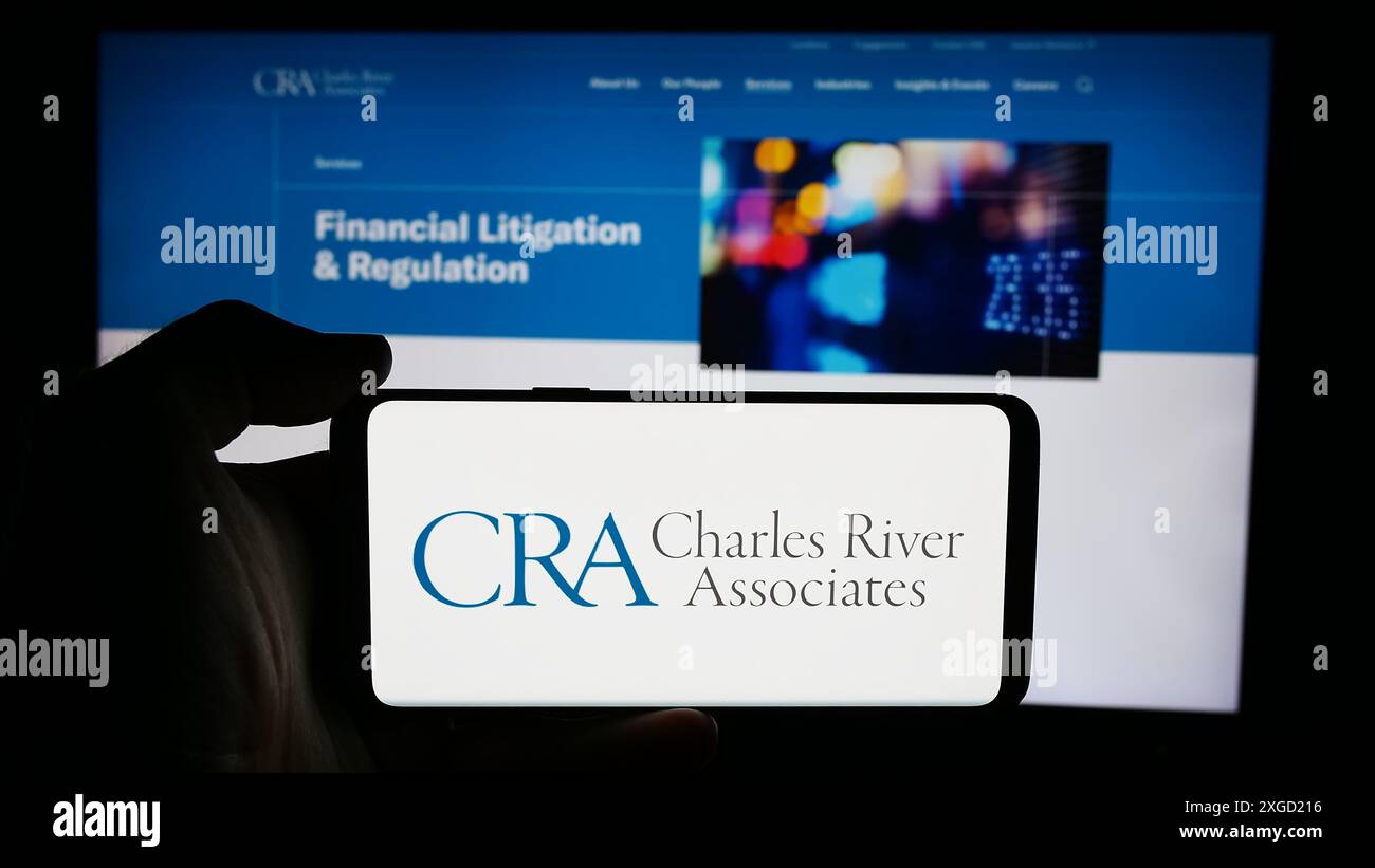 Personne tenant un téléphone cellulaire avec le logo de CRA International Inc (Charles River Associates) devant la page Web de l'entreprise. Concentrez-vous sur l'affichage du téléphone. Banque D'Images
