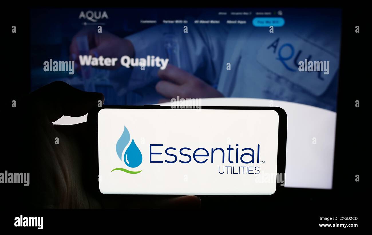 Personne tenant le téléphone portable avec le logo de la société US de services publics de l'eau Essential Utilities Inc en face de la page Web de l'entreprise. Concentrez-vous sur l'affichage du téléphone. Banque D'Images