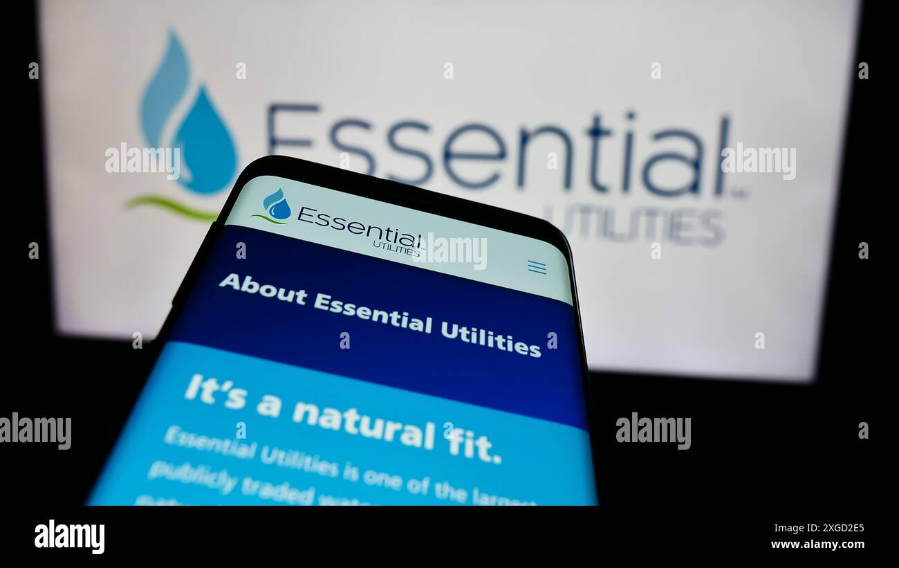 Téléphone portable avec page Web de la société américaine de services publics de l'eau Essential Utilities Inc devant le logo de l'entreprise. Concentrez-vous sur le coin supérieur gauche de l'écran du téléphone. Banque D'Images