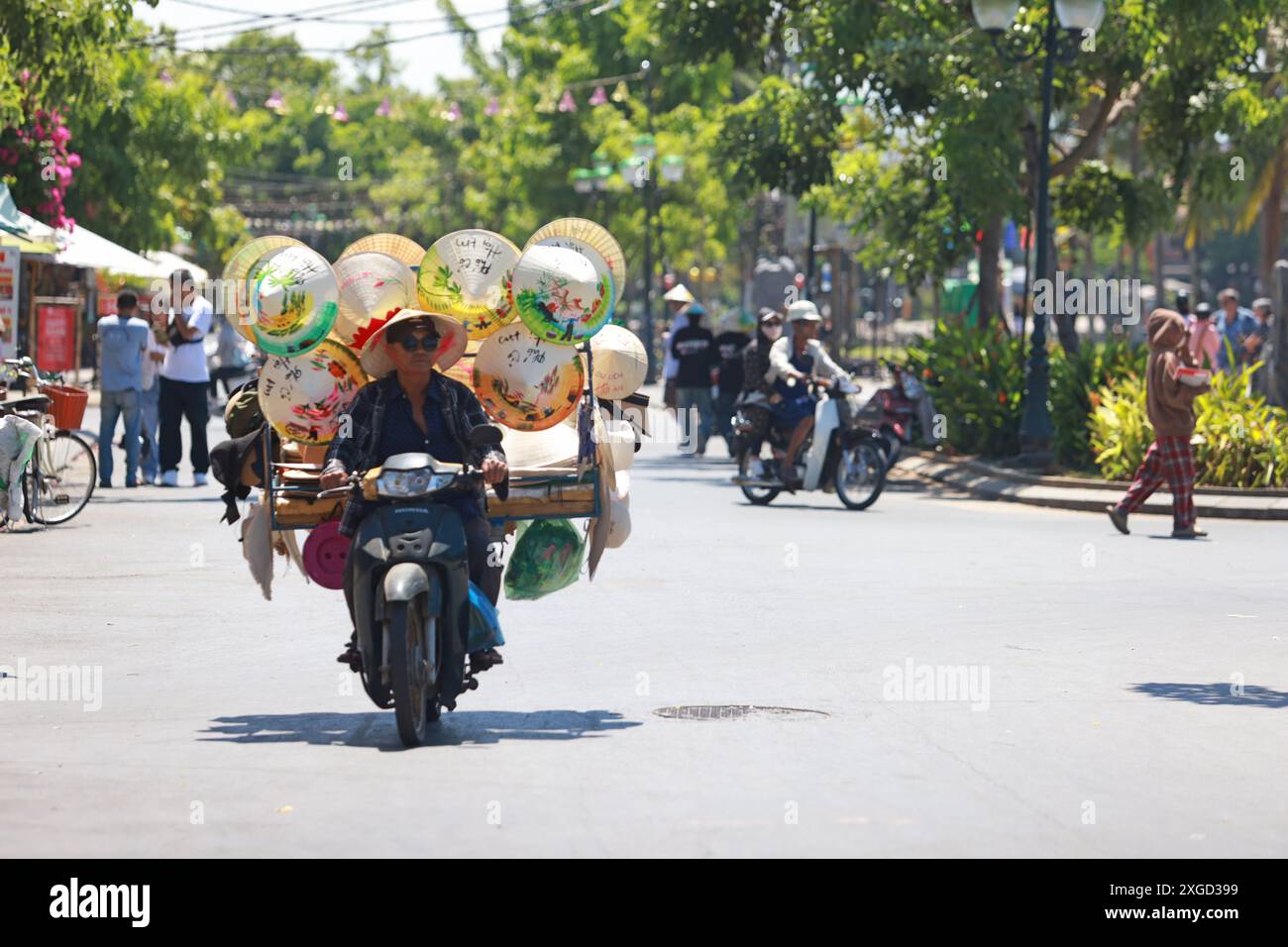 Hoi an, Vietnam 7 juillet 2024 : le colporteur vend ses chapeaux coniques vietness sur la moto. La vieille ville est un port commercial d'Asie du Sud-est datant du 15t Banque D'Images