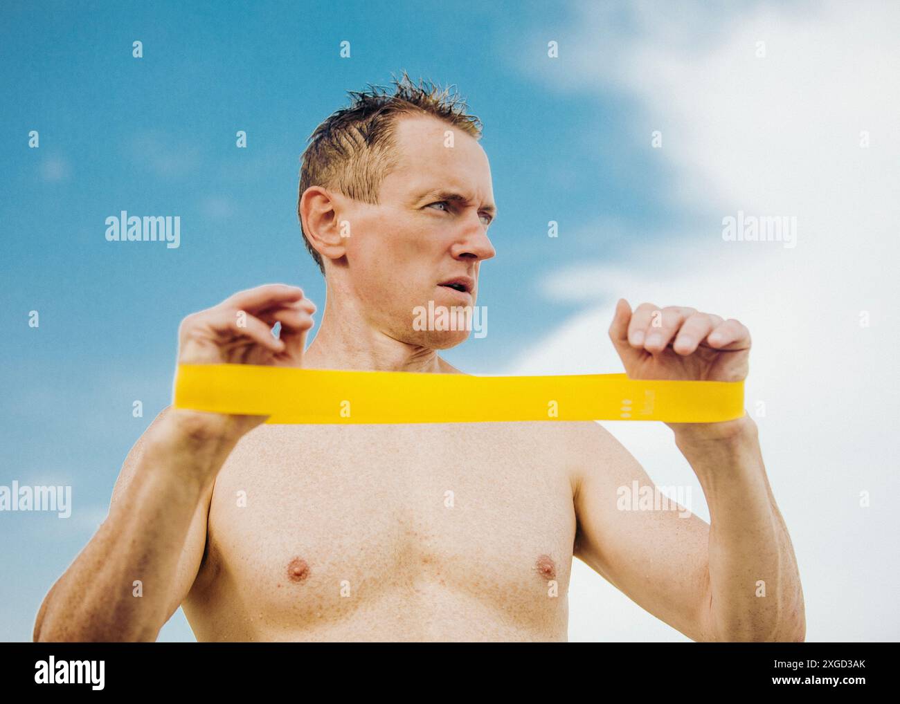 Un homme exerce avec un élastique de fitness sur un fond de ciel bleu Banque D'Images