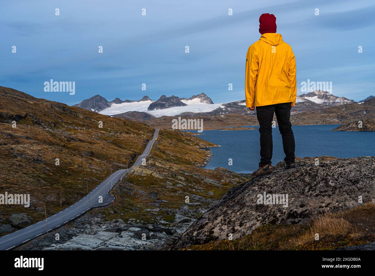 Homme en manteau de pluie jaune regardant le col de montagne, les montagnes glaciaires et les lacs d'eau de fonte, parc national de Jotunheimen, Norvège, Scandinavie, Europe Banque D'Images