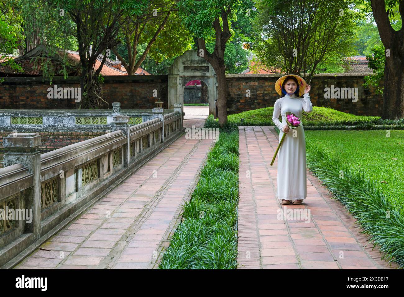 Jolie jeune femme vietnamienne portant une tunique traditionnelle Ao Dai tenant un bouquet de fleurs de lotus au Temple de la littérature, Hanoi, Nord Vietnam, Asie Banque D'Images