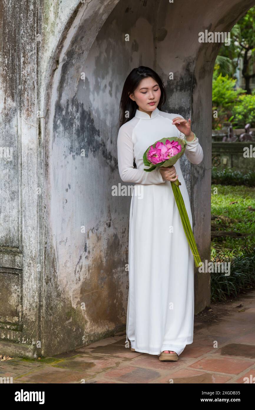 Jolie jeune femme vietnamienne portant une tunique traditionnelle Ao Dai tenant un bouquet de fleurs de lotus au Temple de la littérature, Hanoi, Nord Vietnam, Asie Banque D'Images