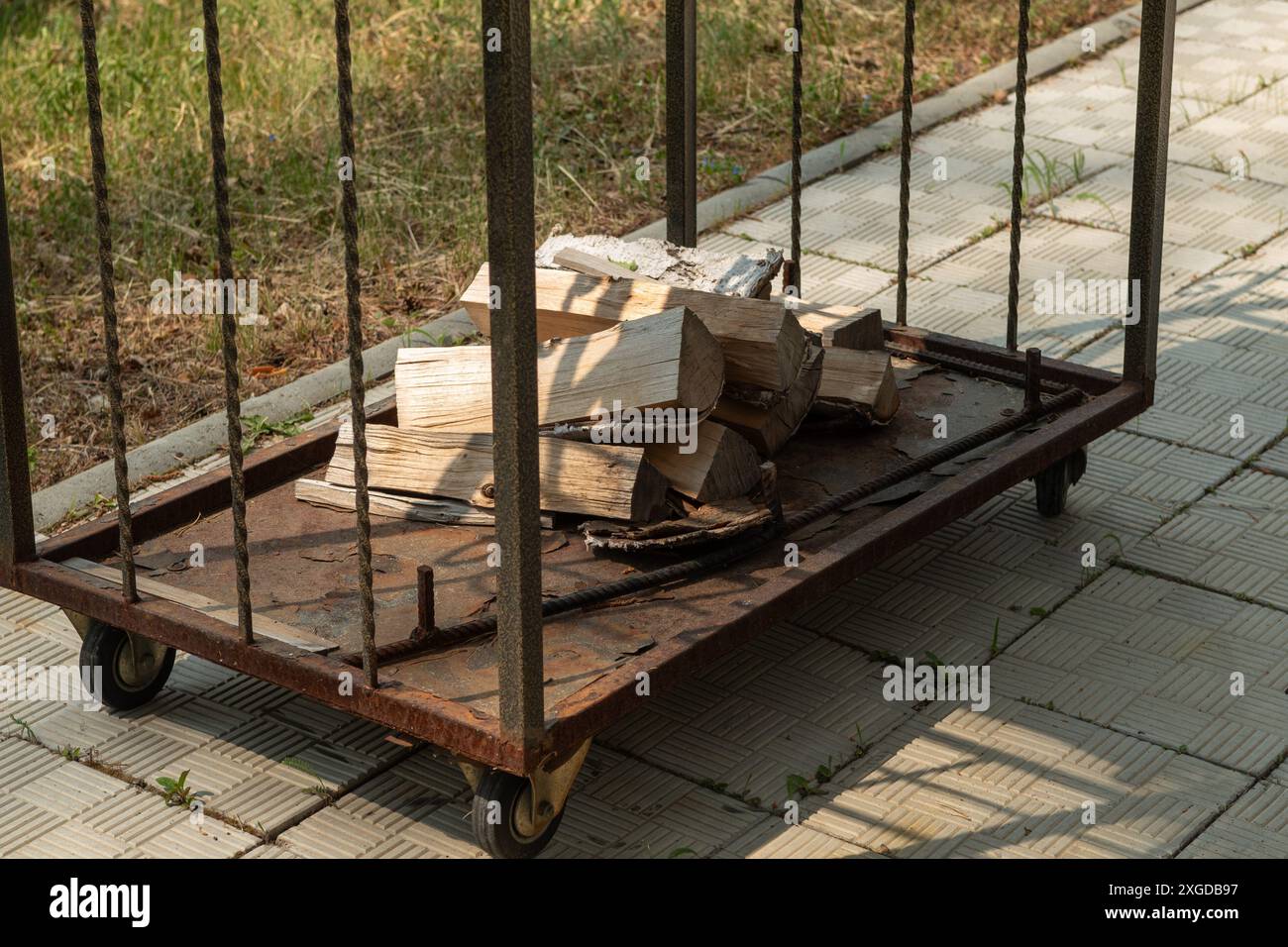 Un chariot de bois de chauffage antique, altéré par le temps, sur le trottoir à côté d'une pelouse luxuriante. Le chariot rustique à quatre roues porte du bois de chauffage haché, servant Banque D'Images