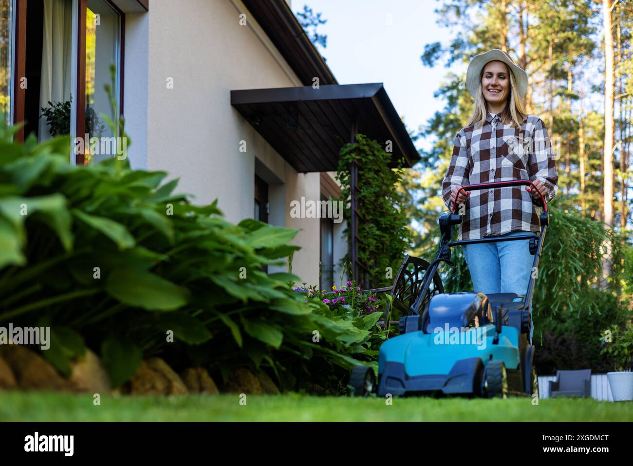 femme fauchant l'herbe avec tondeuse à gazon électrique au jardin de la maison Banque D'Images