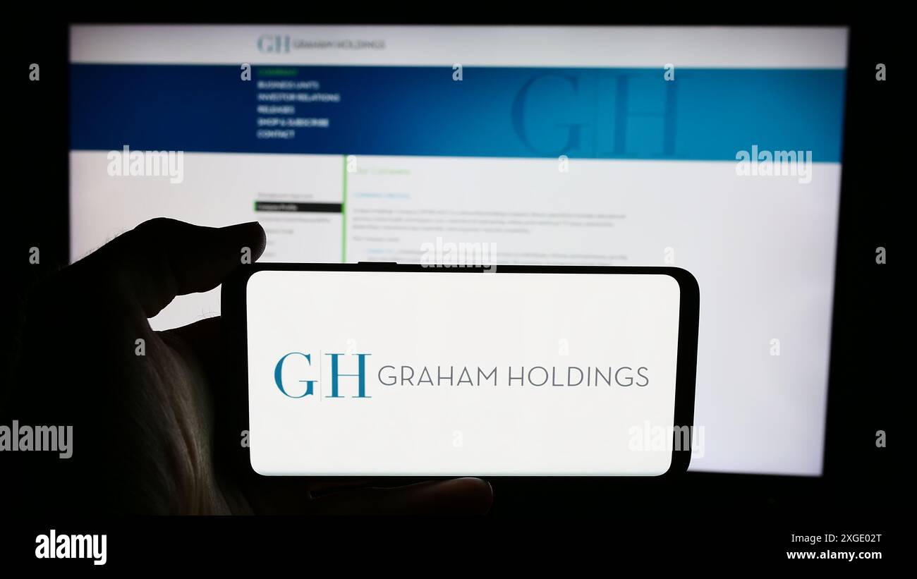 Personne tenant un téléphone portable avec le logo de l'entreprise de médias américaine Graham Holdings Company devant la page Web de l'entreprise. Concentrez-vous sur l'affichage du téléphone. Banque D'Images