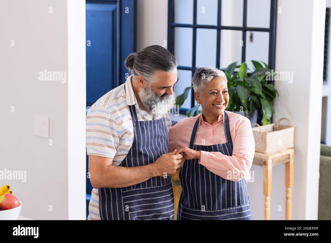 Couple senior portant des tabliers souriant et se tenant les mains dans la cuisine Banque D'Images