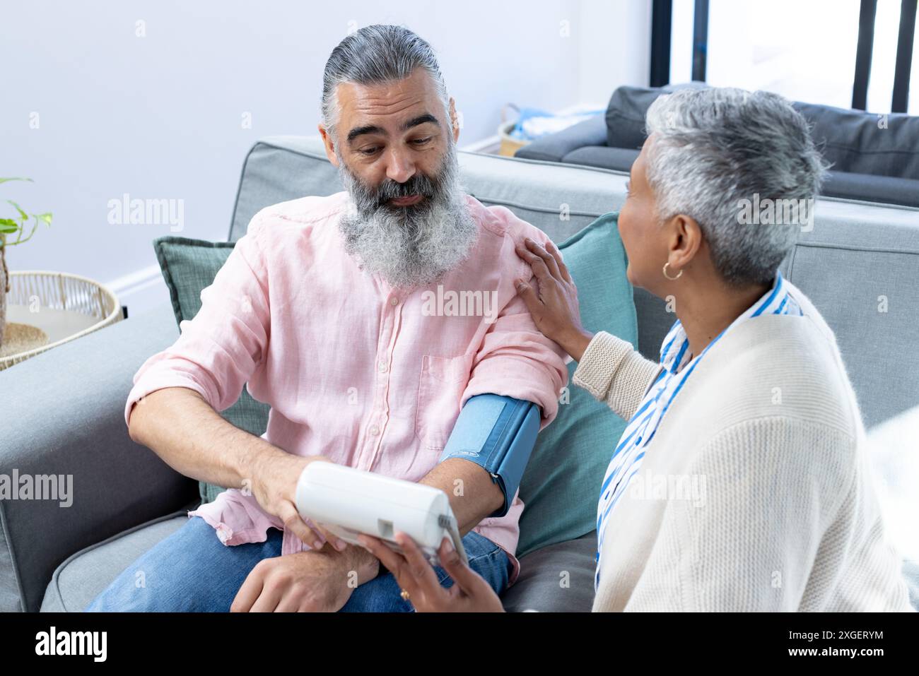 Vérification de la pression artérielle, homme senior assis sur le canapé avec la femme aidant Banque D'Images