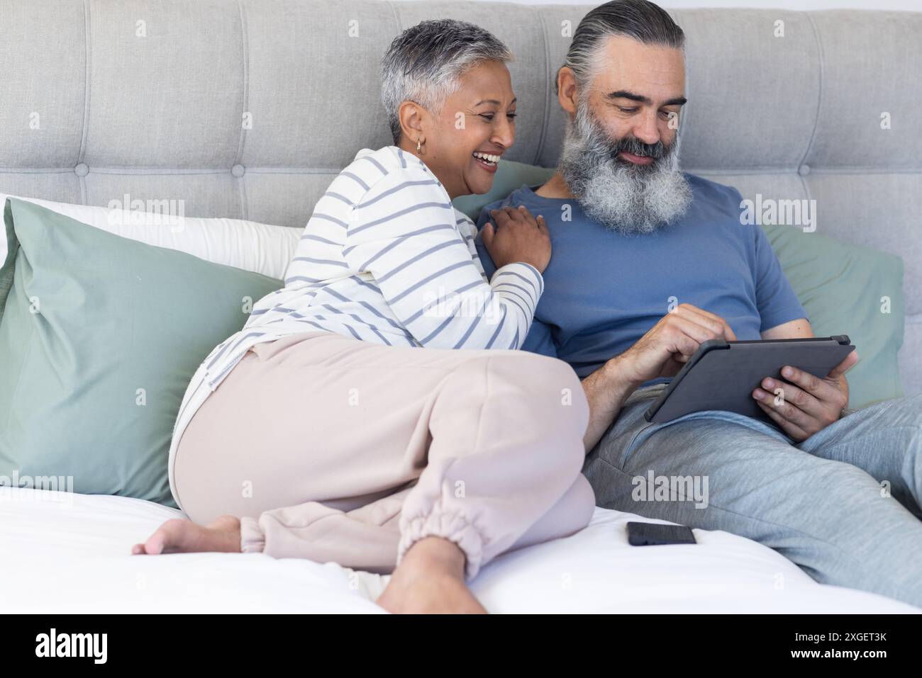 Couple senior se relaxant sur le lit, en utilisant la tablette et en souriant ensemble Banque D'Images