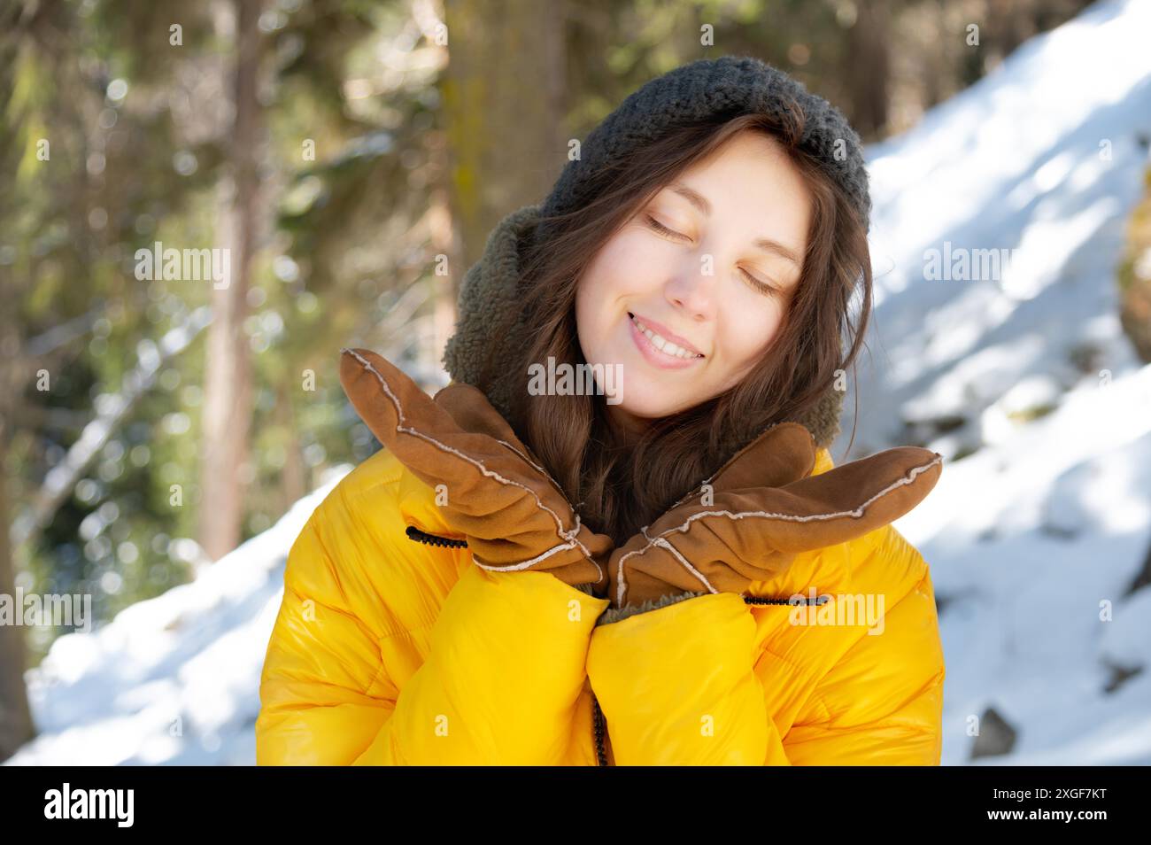 Heureuse jeune femme caucasienne dans un chapeau de veste en duvet d'hiver et des mitaines avec les yeux fermés. avec le bonheur se réjouit de répandre ses mains en hiver Banque D'Images