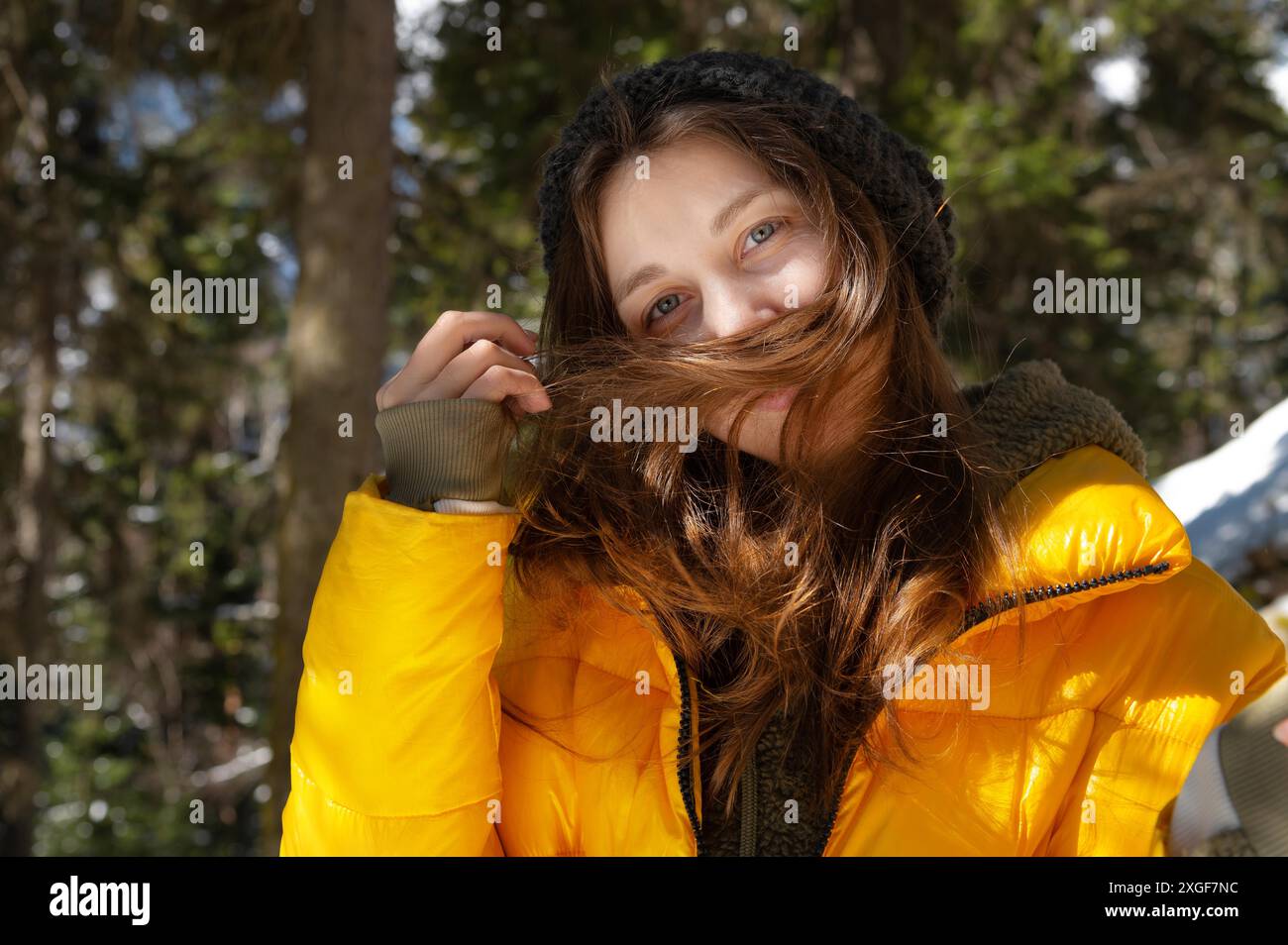Heureuse jeune femme caucasienne dans un chapeau de veste en duvet d'hiver et des mitaines avec bonheur se réjouit de répandre ses mains dans une forêt de conifères d'hiver Banque D'Images