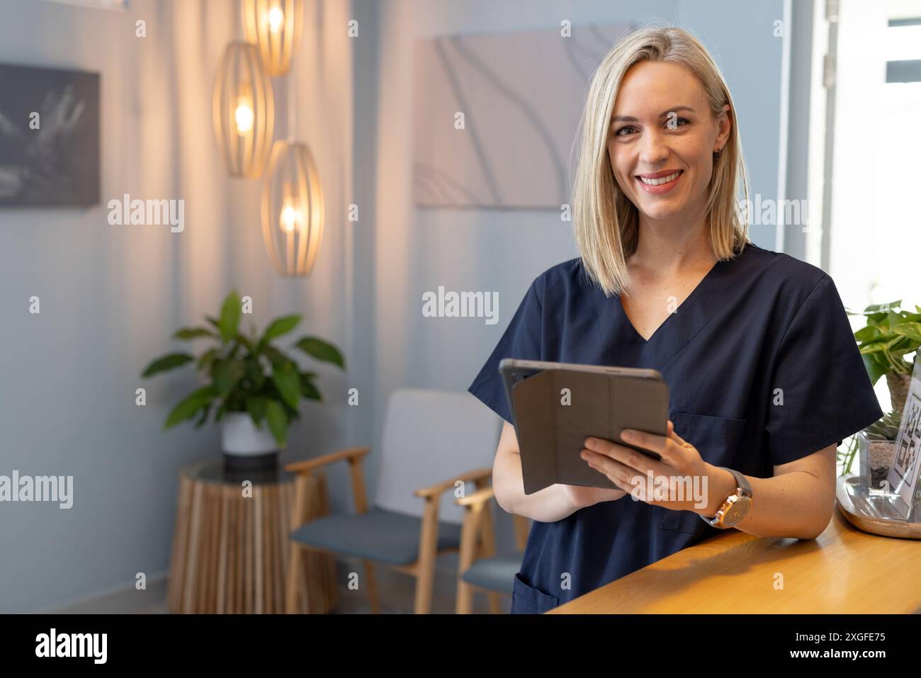 Femme souriante dans les gommages tenant la tablette, debout dans la zone de réception de la clinique médicale, espace de copie Banque D'Images