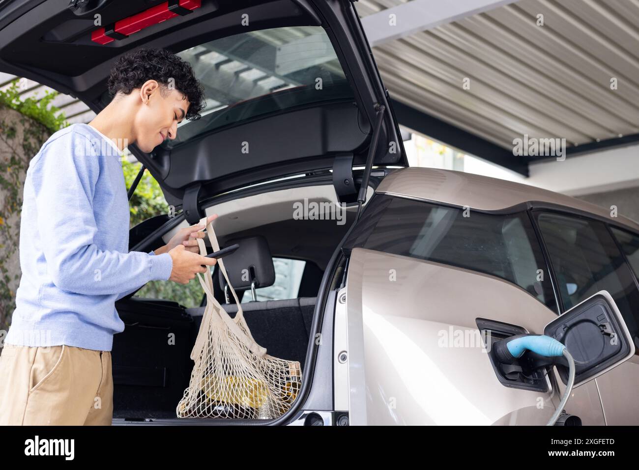 Chargement de l'épicerie dans la voiture électrique, homme utilisant le sac réutilisable dans le garage Banque D'Images