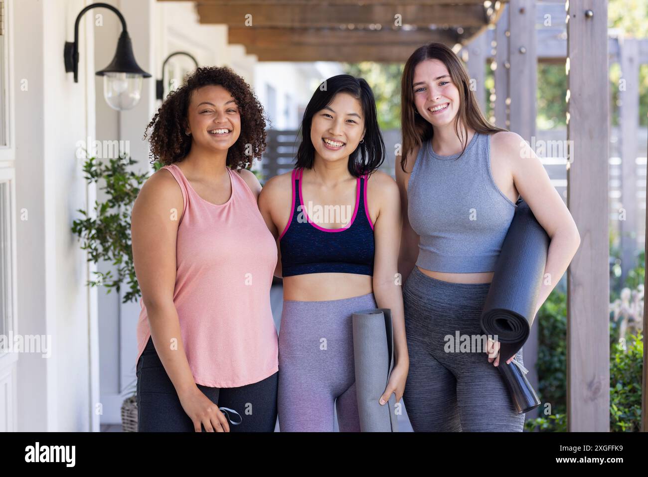 Tenant des tapis de yoga, trois amies femmes souriant et posant après la séance d'entraînement à la maison Banque D'Images