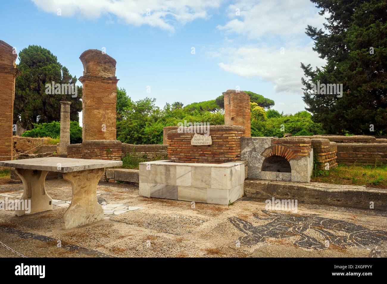 Macellum e Tabernae dei Pescivendoli - le Macellum est accessible depuis le Decumanus par une entrée avec des colonnes sur les côtés de laquelle, dans la première moitié du IIIe siècle après JC, deux tabernae (magasins) ont été créés, dotés de comptoirs pour la vente de poissons et de bassins en marbre. La salle de gauche conserve une mosaïque représentant un dauphin mangeant un calmar, avec l’inscription « Inbide te calco » (« créature envieuse, je te piétinerai »), car on pensait que les dauphins perturbaient la pêche.- Parc archéologique d’Ostie Antica, Rome, Italie Banque D'Images