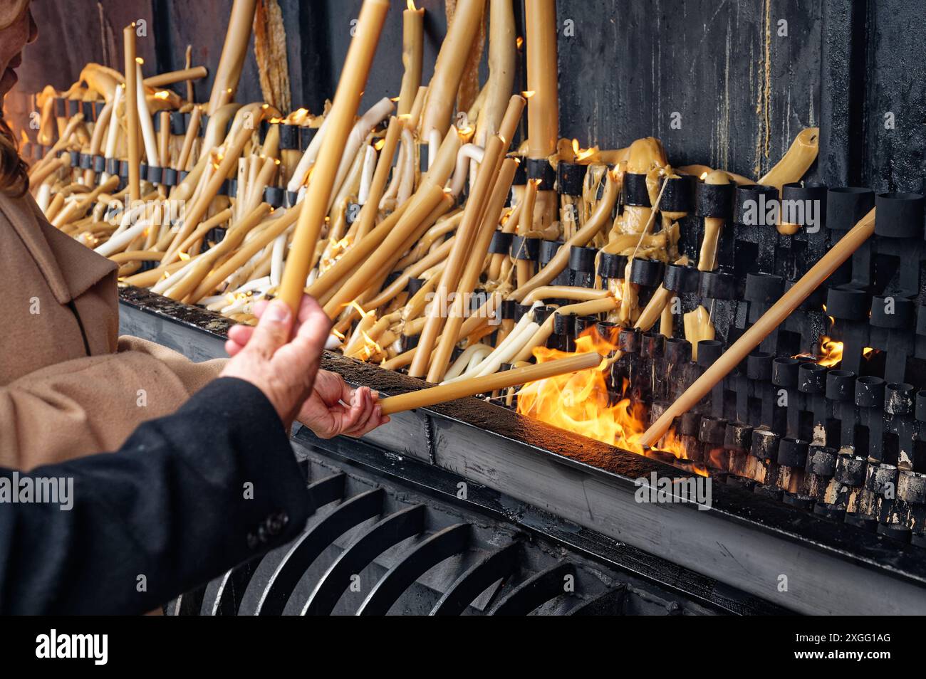 Au sanctuaire de fatima, les visiteurs allument de grandes bougies, leurs mains plaçant soigneusement les mèches dans les flammes Banque D'Images