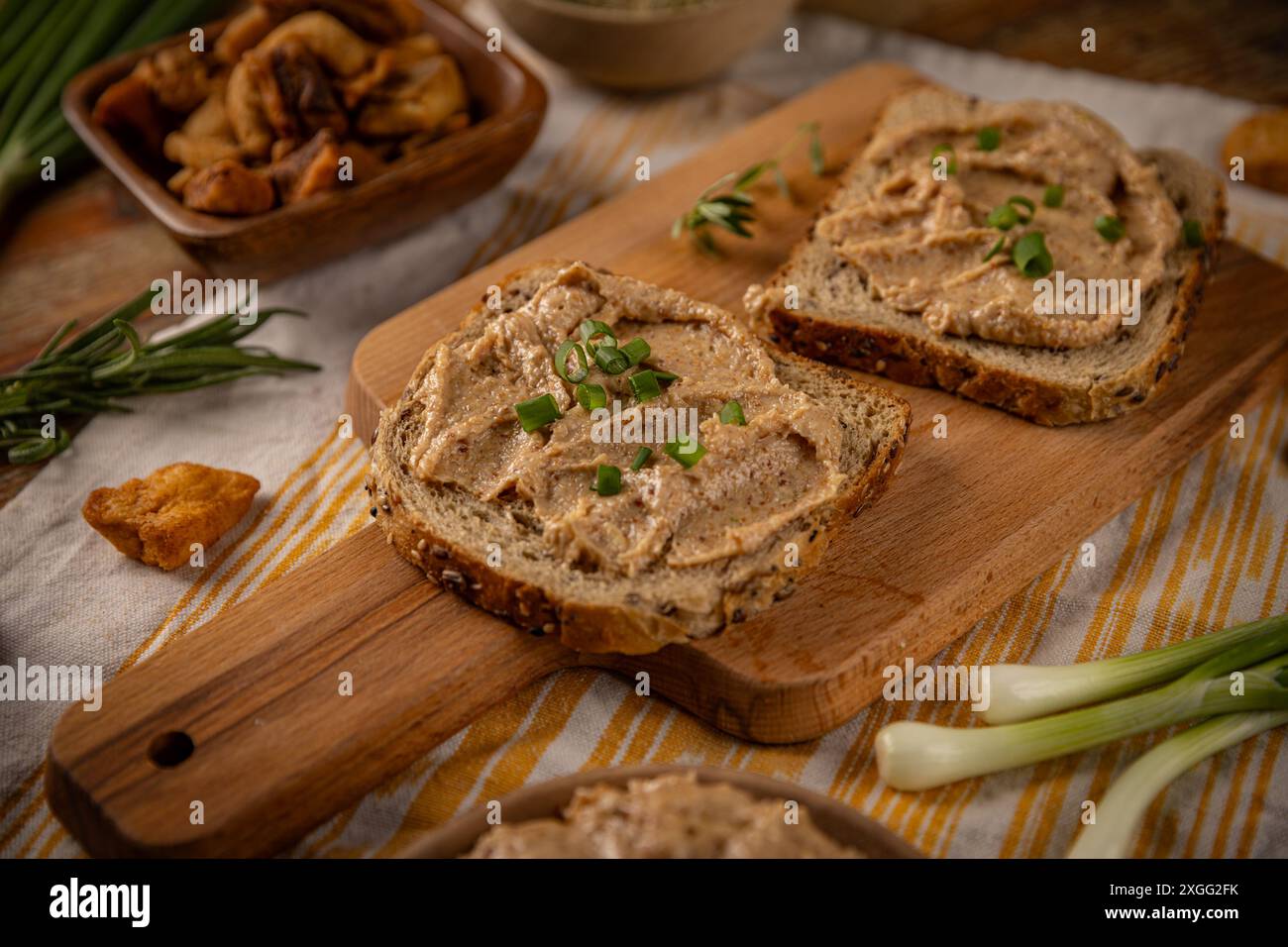 Deux tranches de pain grillé avec tartinade et ciboulette couchées sur une planche de bois, romarin et cretons autour Banque D'Images