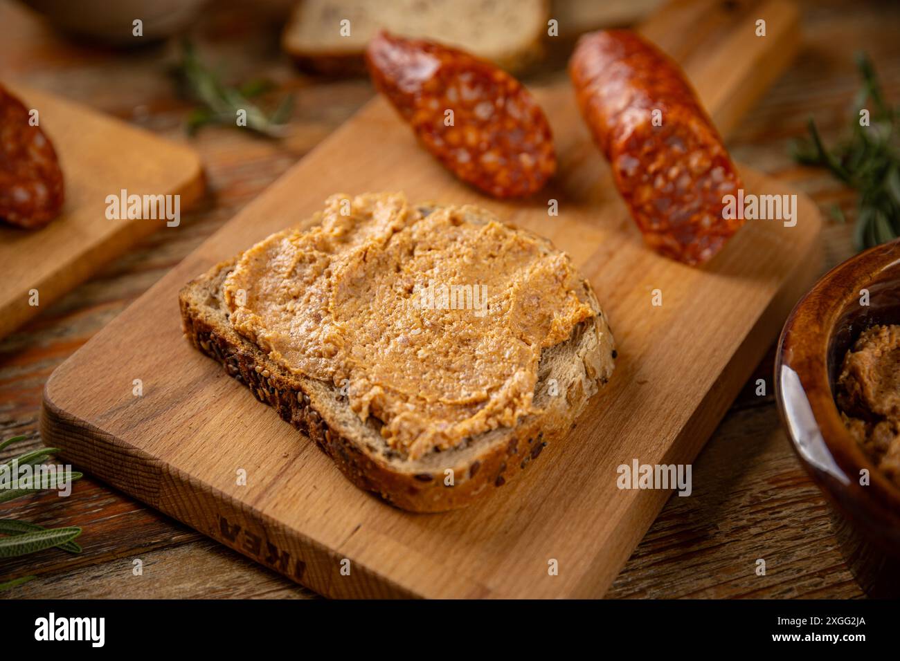 Tranches de saucisse couchées sur une planche à découper près du pain avec tartinade Banque D'Images