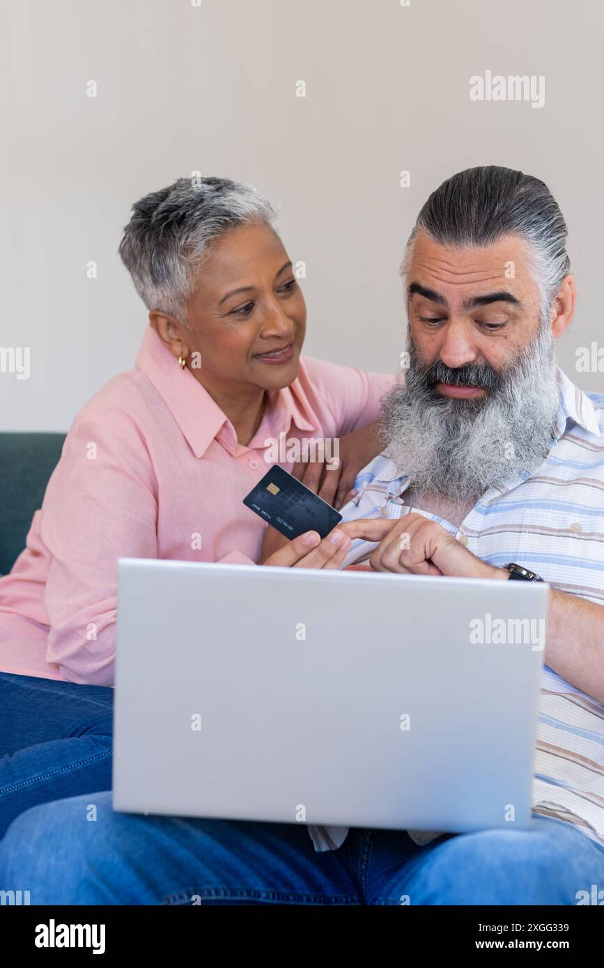 En utilisant un ordinateur portable, couple senior tenant la carte de crédit et discutant de l'achat en ligne Banque D'Images En utilisant un ordinateur portable, couple senior tenant la carte de crédit et discutant de l'achat en ligne Banque D'Images
