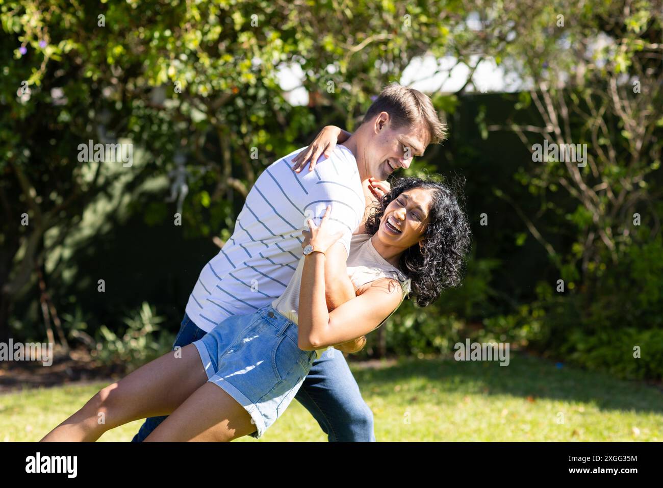 Jeune couple dansant et riant ensemble dans le jardin extérieur ensoleillé Banque D'Images