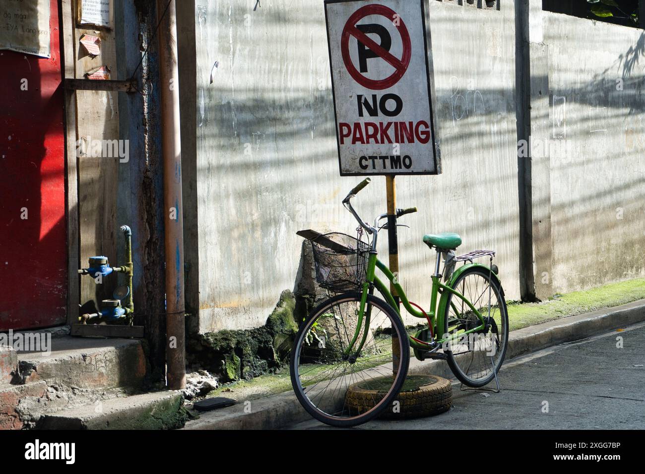 Un vélo vert est garé à côté d'un panneau de stationnement interdit. Le panneau est sur un poteau et se trouve devant un bâtiment Banque D'Images