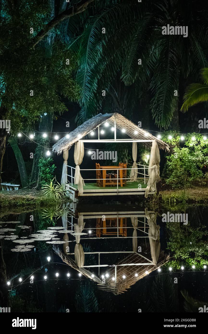 Pergola avec des lumières incandescentes au bord de l'eau. Gazebo avec lumières au bord du lac en fin de soirée. Scène romantique au crépuscule. Patio romantique dans la soirée. Nuit Banque D'Images