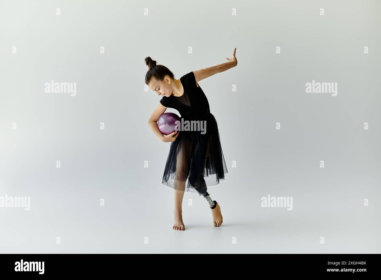 Une jeune fille avec une jambe prothétique effectue une routine de gymnastique avec une balle violette. Banque D'Images