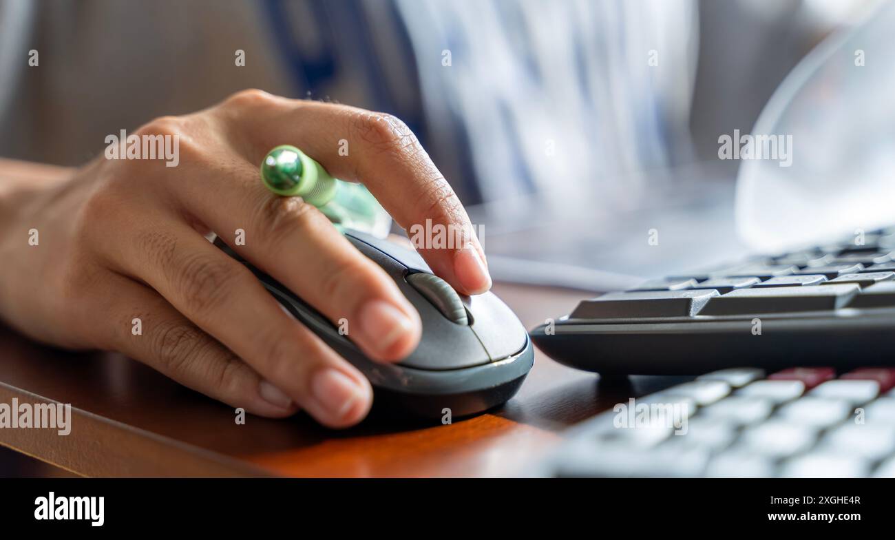 Femme utilisant la souris PC tout en travaillant sur l'ordinateur à la table. Gros plan sur la main de la jeune femme assise à la table en bois dans le bureau tenant la souris de la Banque D'Images