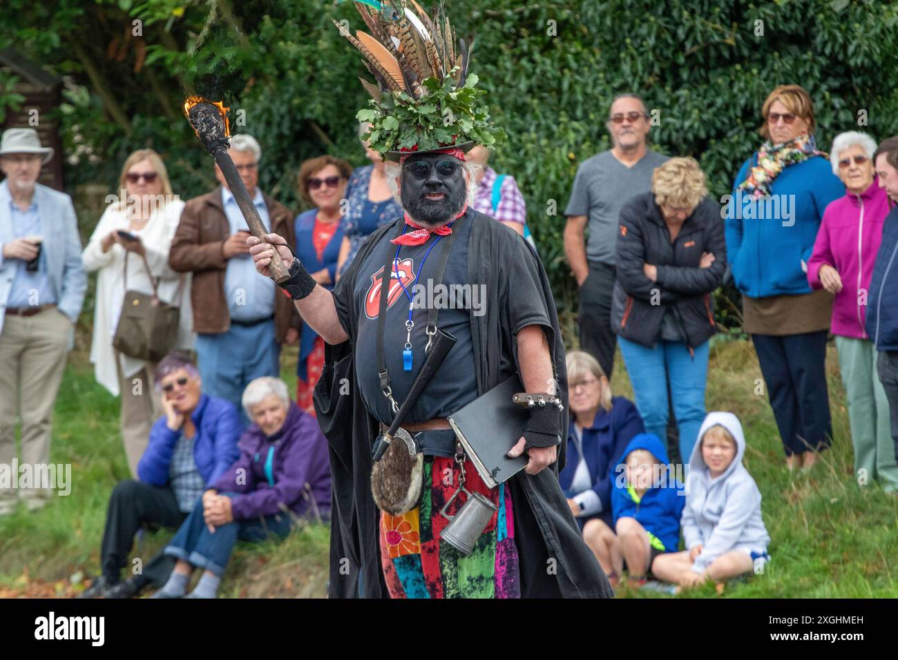 Le chef du Rendham Mummers Suffolk en face noire traditionnelle et tenant une torche flamboyante se produisant sur la route pour le solstice d'été Banque D'Images