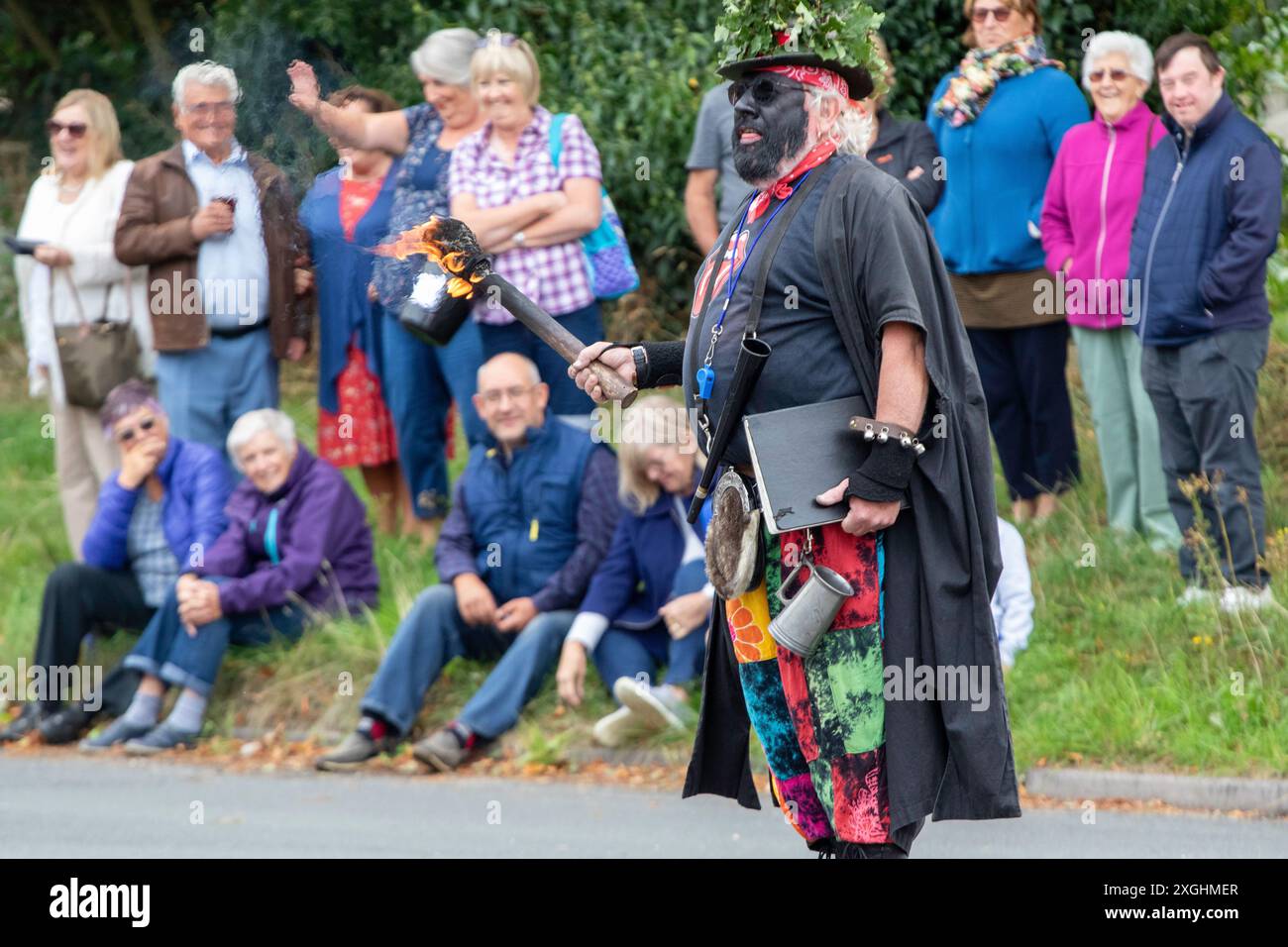 Le chef du Rendham Mummers Suffolk en face noire traditionnelle et tenant une torche flamboyante se produisant sur la route pour le solstice d'été Banque D'Images