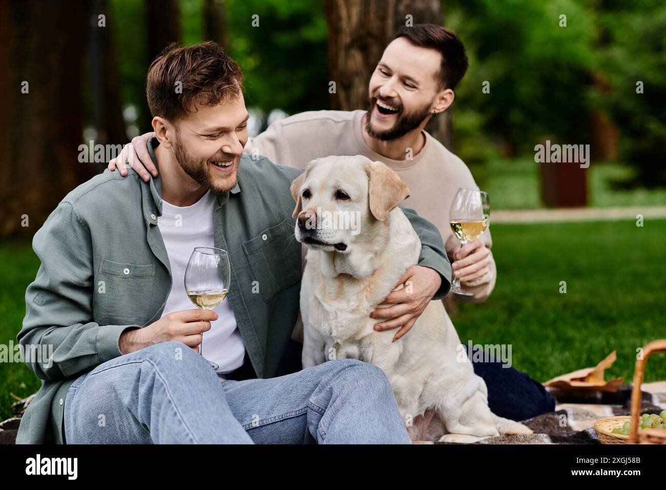 Un couple gay barbu profite d'un pique-nique avec son chien labrador dans un parc verdoyant. Banque D'Images