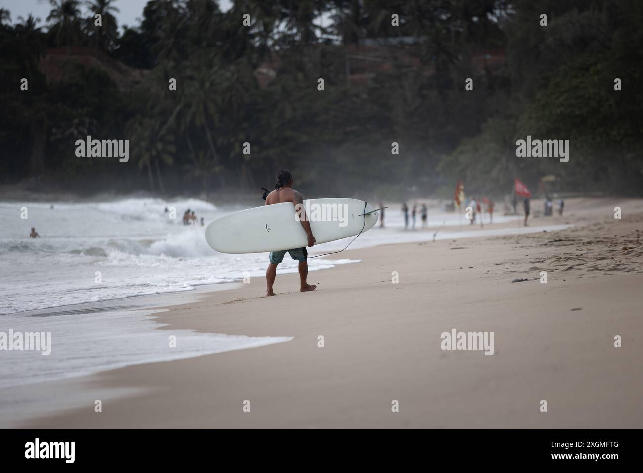 Un surfeur avec sa planche de surf marchant sur la plage de Phuket Thaïlande. Cours de surf à Phuket. Cours de surf à Phuket. Juillet 7,2024 Banque D'Images