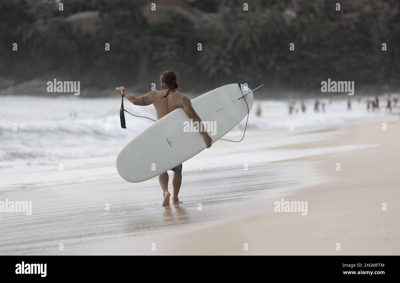 Un surfeur avec sa planche de surf marchant sur la plage de Phuket Thaïlande. Cours de surf à Phuket. Cours de surf à Phuket. Juillet 7,2024 Banque D'Images