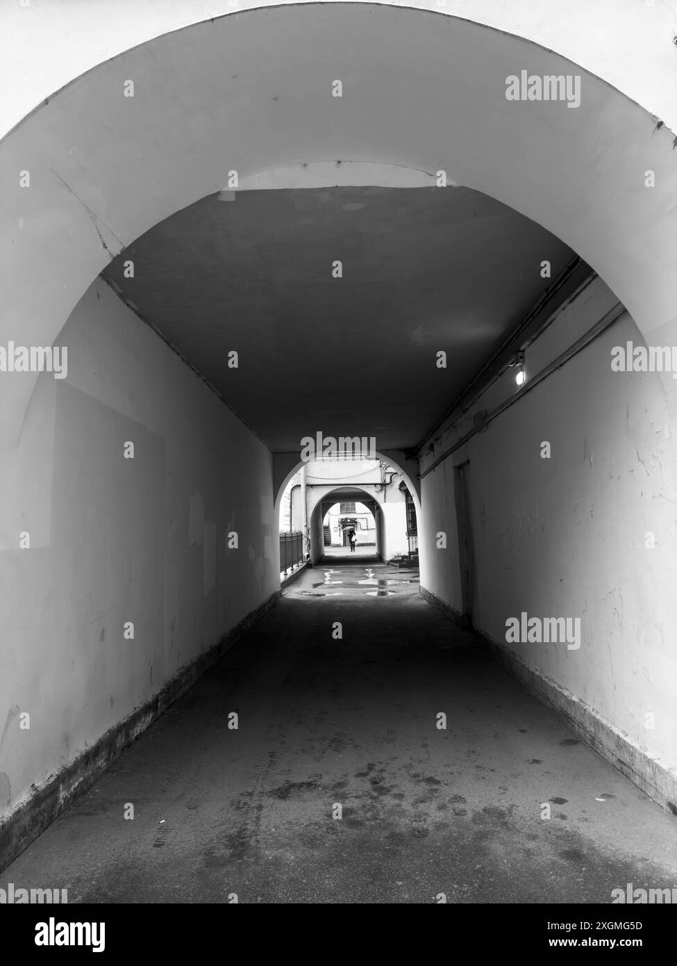 Image monochrome d'un tunnel avec des passages voûtés, menant à une personne marchant au loin. Moody et scène architecturale. Banque D'Images