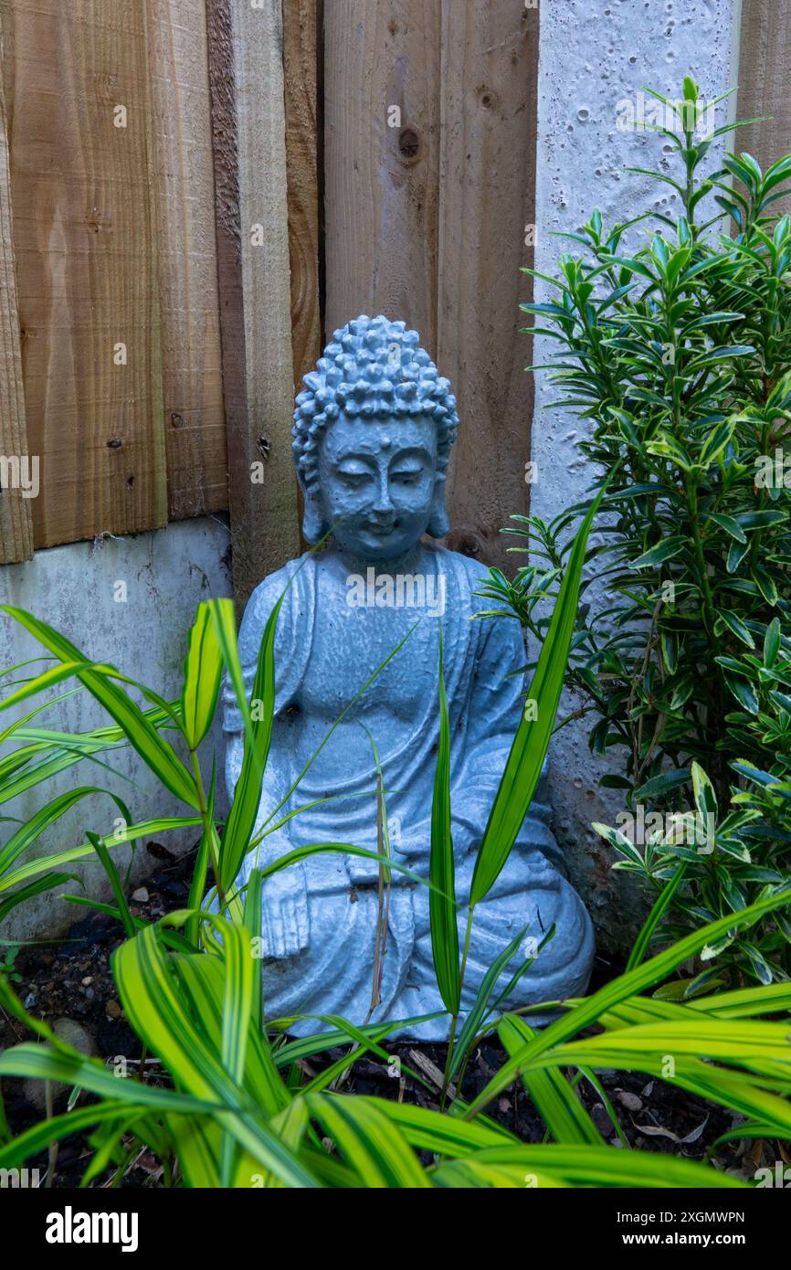 Une image en gros plan d'une statue de Bouddha en pierre grise assise au milieu d'un jardin animé. Banque D'Images