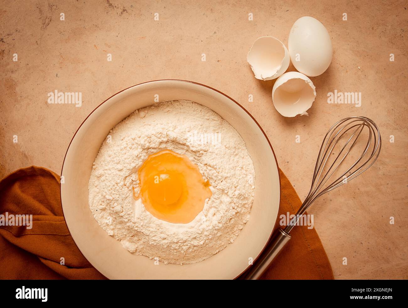 Fond alimentaire, concept, assiette avec farine de blé, oeuf cassé, fouet, serviette de cuisine, sur une table beige, vue de dessus, rustique Banque D'Images