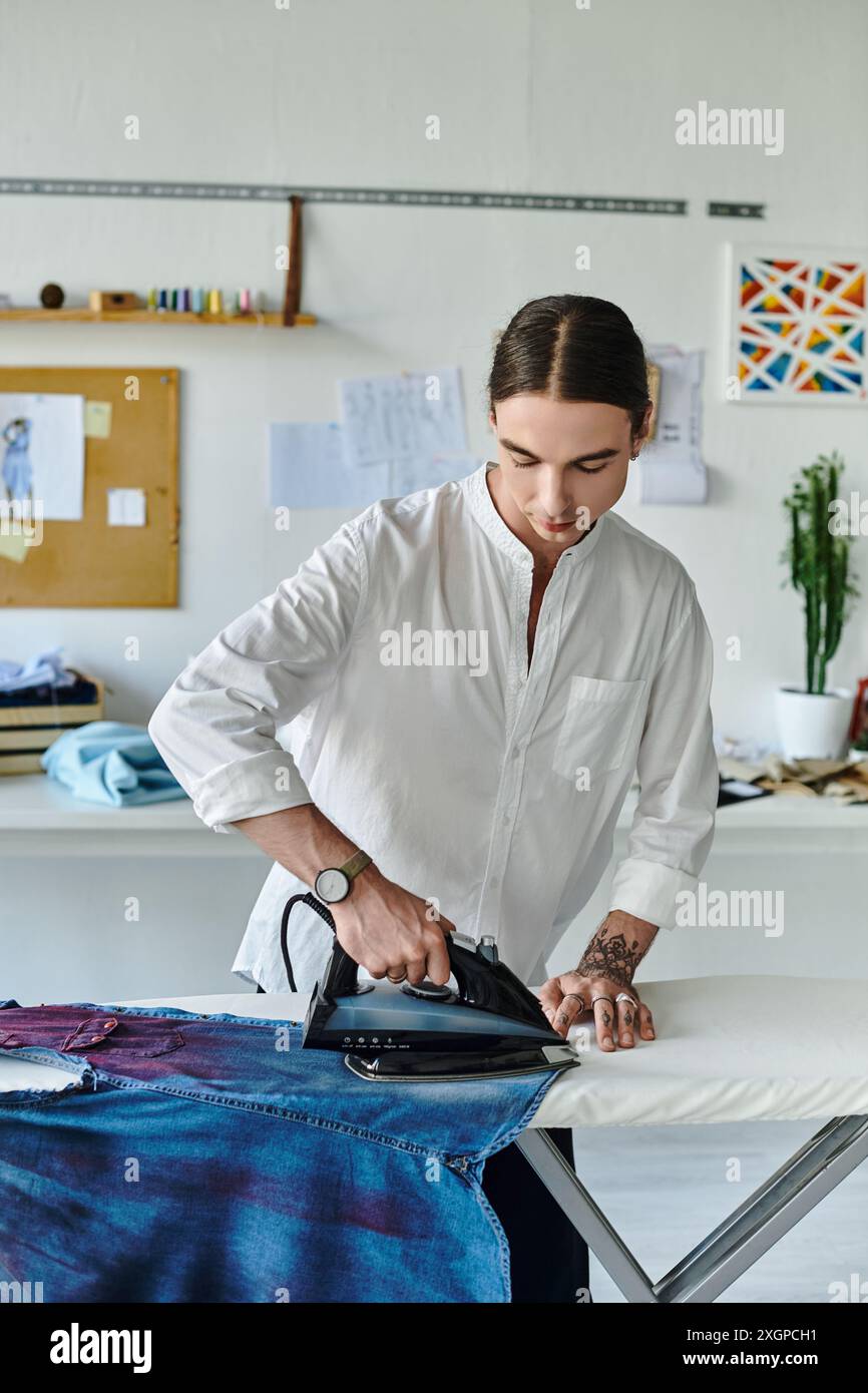 Un jeune homme repasse méticuleusement une paire de jeans denim dans son atelier de restauration de vêtements. Banque D'Images